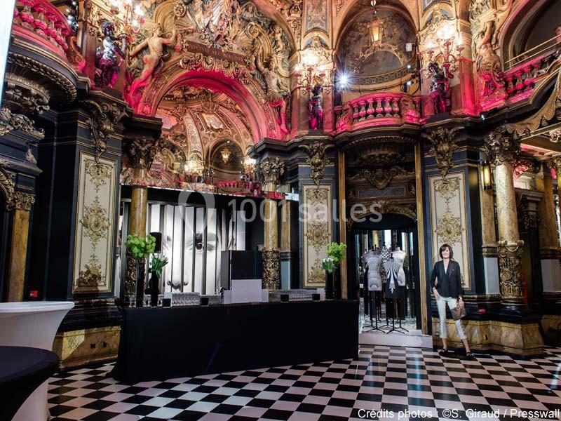Intérieur d'une salle richement décorée avec des ornements dorés, un sol en damier et un espace d'exposition moderne.