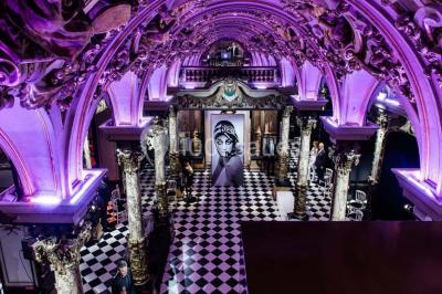 Salle élégante avec tables rondes dressées, chaises blanches et grand portrait en noir et blanc en arrière-plan.
