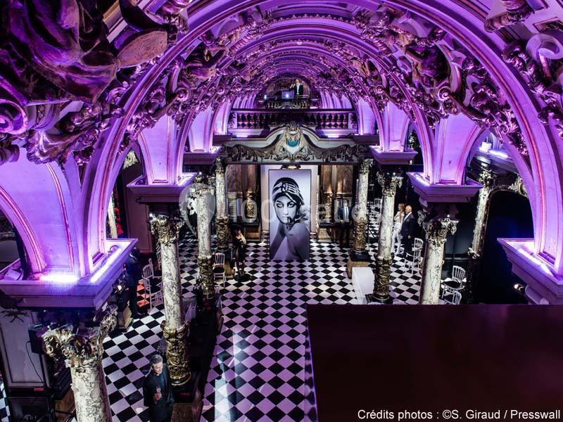 Intérieur d'une salle ornée de colonnes sculptées et éclairée en violet, avec un sol en damier noir et blanc.
