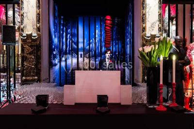 Salle élégante avec tables rondes dressées, chaises blanches et grand portrait en noir et blanc en arrière-plan.