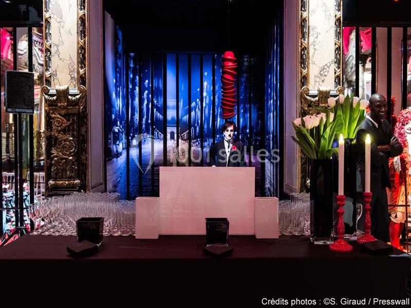 Un homme en costume se tient derrière un comptoir blanc, entouré de verres et de décorations élégantes.