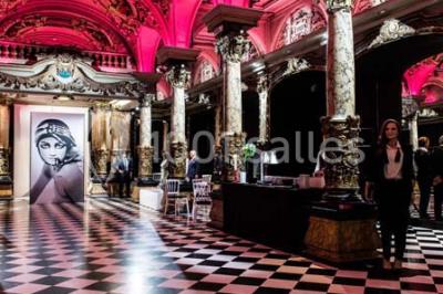 Salle élégante avec tables rondes dressées, chaises blanches et grand portrait en noir et blanc en arrière-plan.