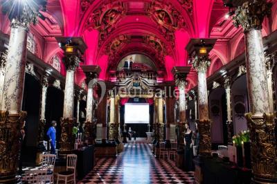Salle élégante avec tables rondes dressées, chaises blanches et grand portrait en noir et blanc en arrière-plan.