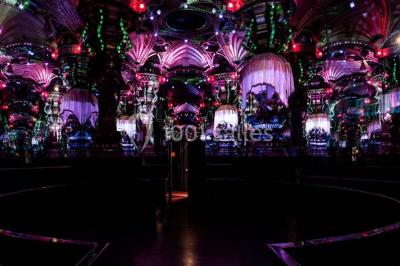 Salle élégante avec tables rondes dressées, chaises blanches et grand portrait en noir et blanc en arrière-plan.