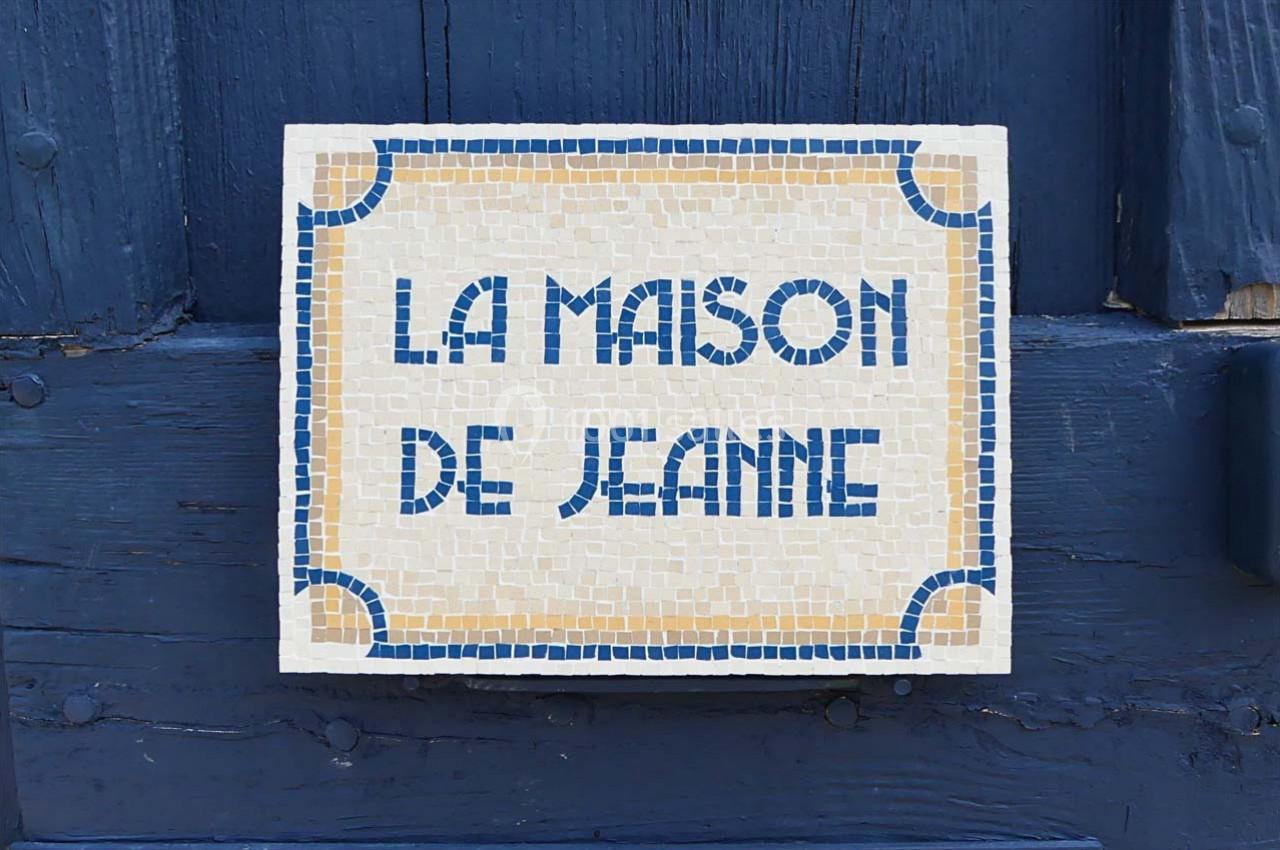 Plaque en mosaïque avec l'inscription ’La Maison de Jeanne’ fixée sur une porte en bois bleu.