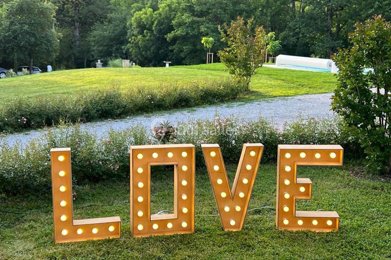 Lettres lumineuses formant le mot ’LOVE’ installées sur une pelouse, avec un parc verdoyant en arrière-plan.