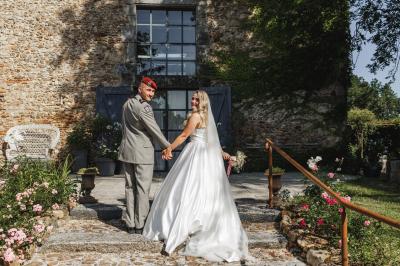 Allée de gravier bordée de rosiers roses en fleurs, entourée de pelouse et d'arbres en arrière-plan.