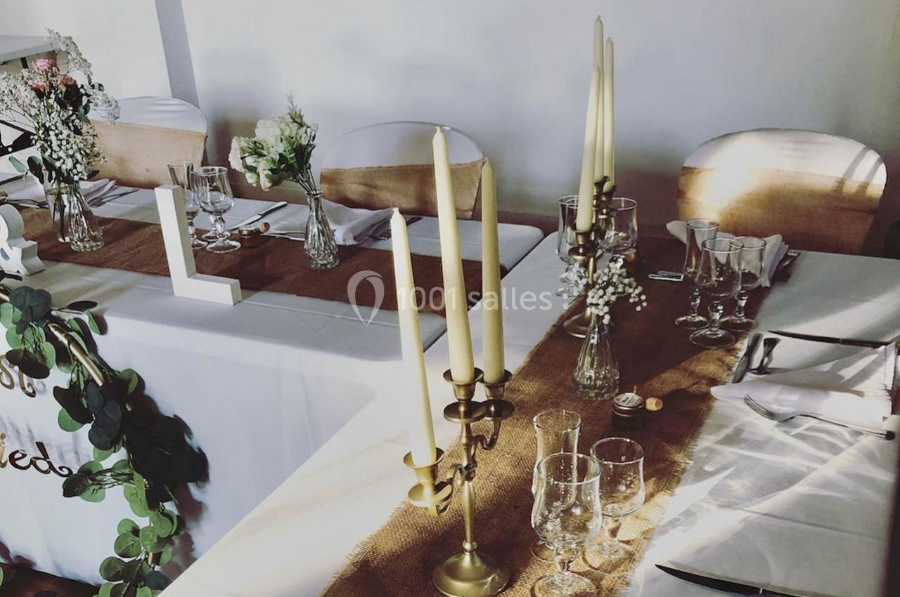 Table décorée pour un événement avec nappes blanches, chemin de table en toile de jute, chandeliers et fleurs.