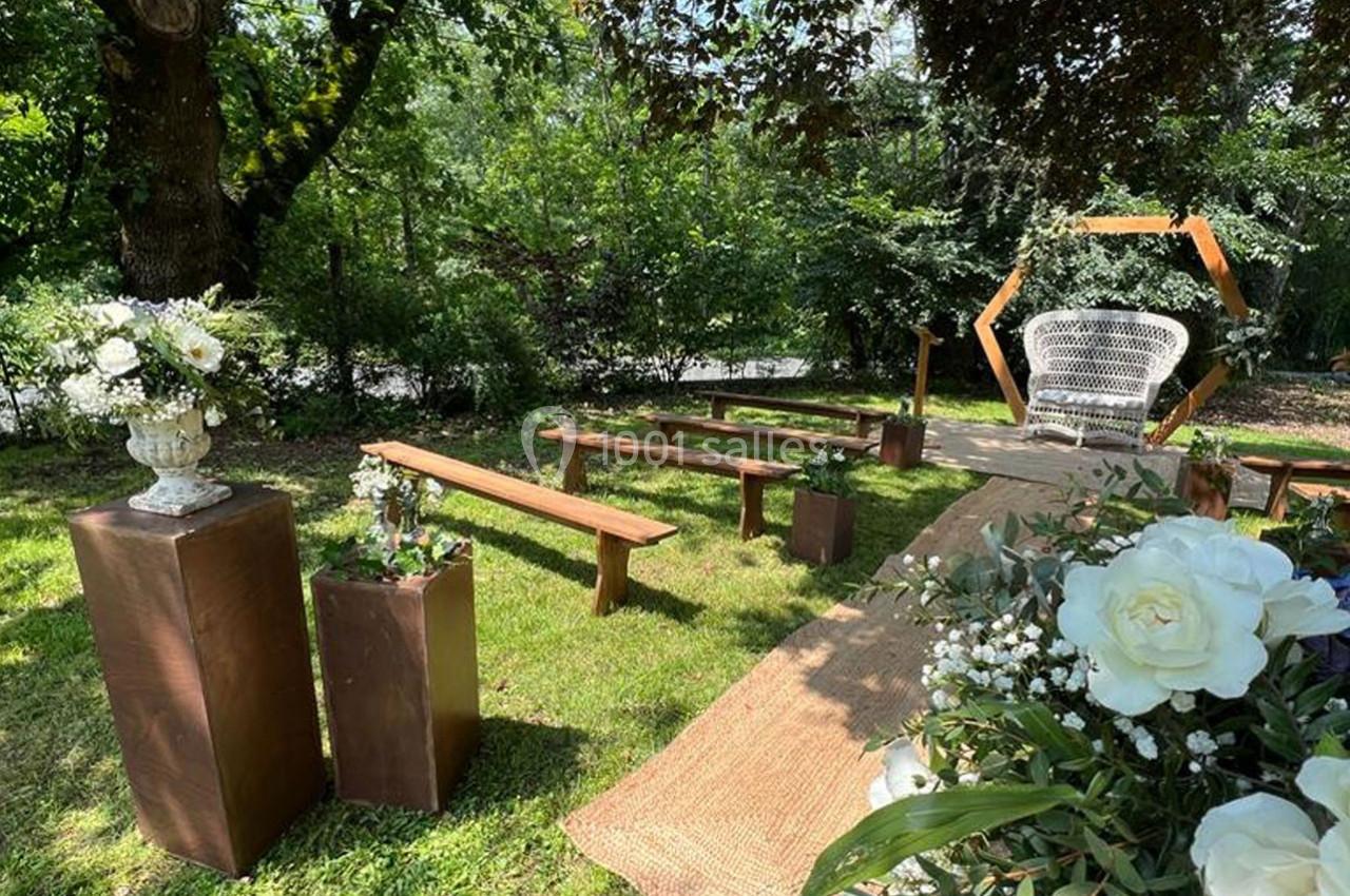 Allée décorée pour une cérémonie en extérieur avec bancs en bois, fleurs blanches et arche géométrique en arrière-plan.