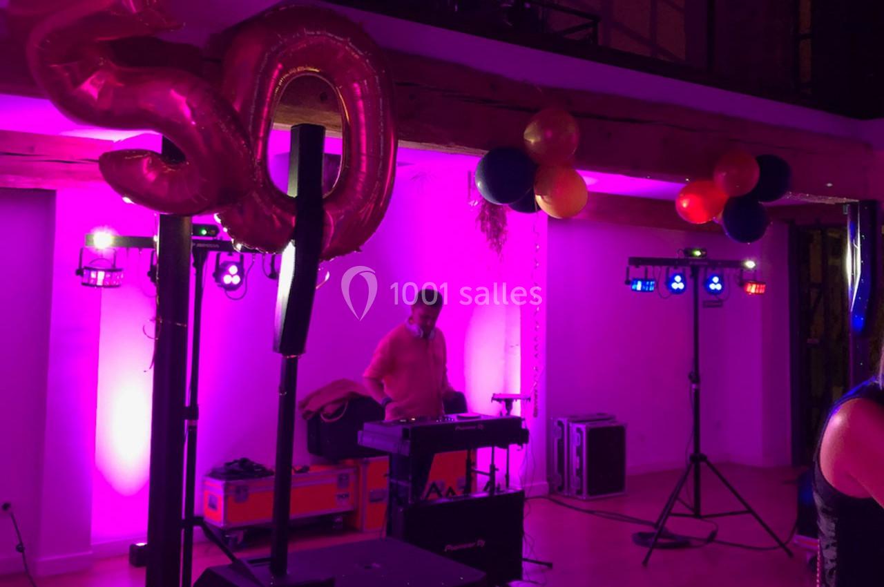 Un DJ anime une soirée d'anniversaire avec des ballons et une décoration lumineuse rose et violette.