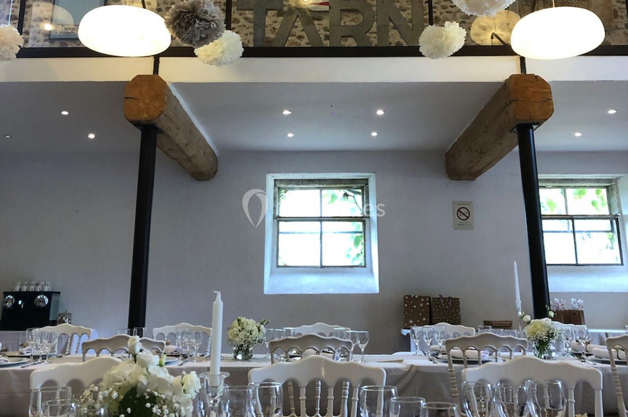 Salle de réception décorée avec des tables dressées, des fleurs blanches et des suspensions en papier au plafond.