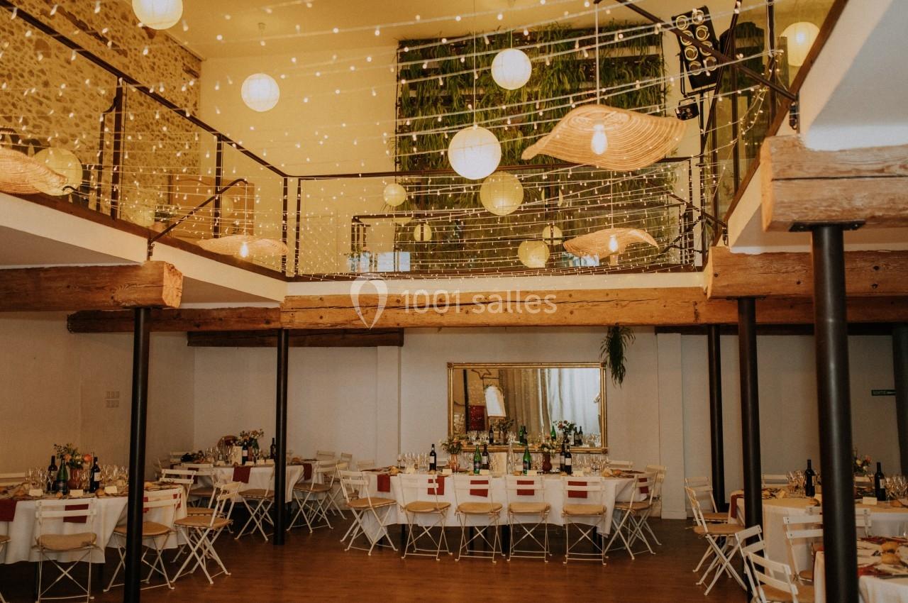 Salle de réception décorée avec des guirlandes lumineuses, des tables dressées et un mur végétal en arrière-plan.