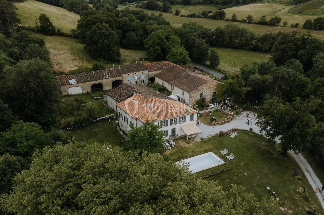 Vue aérienne d'une grande maison en pierre avec piscine, entourée de verdure et de bâtiments annexes dans un paysage rural.