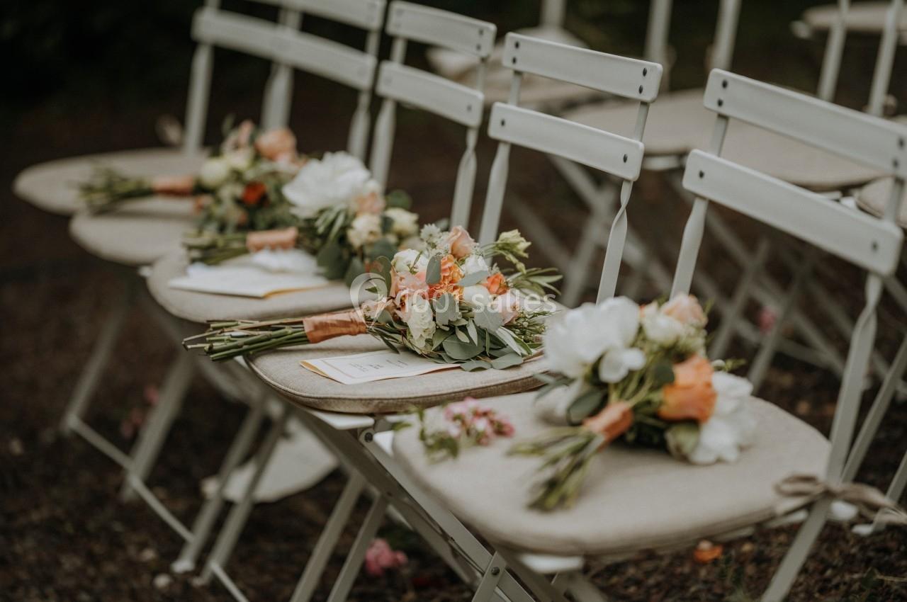 Chaises blanches alignées en extérieur, décorées de bouquets de fleurs aux tons pastel posés sur les assises.