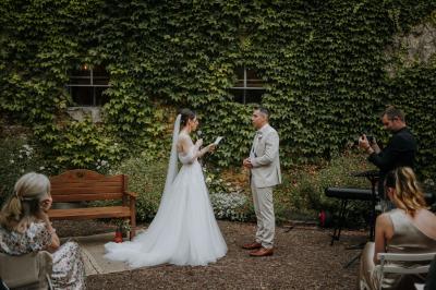 Allée de gravier bordée de rosiers roses en fleurs, entourée de pelouse et d'arbres en arrière-plan.