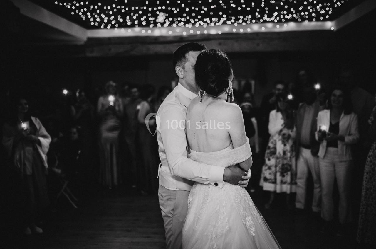 Un couple danse sous des lumières suspendues, entouré d'invités dans une ambiance festive en noir et blanc.