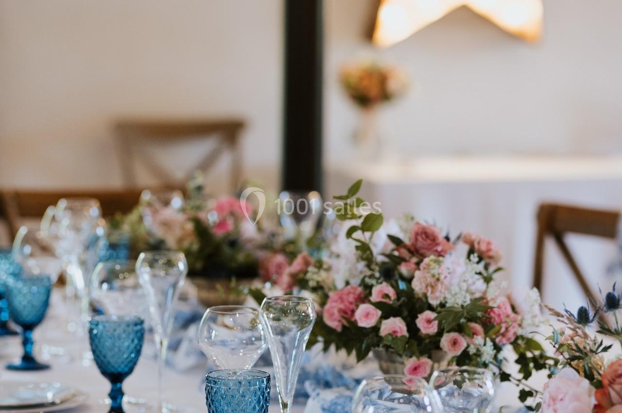 Table élégamment dressée avec vaisselle bleue, bouquets de fleurs roses et étoile lumineuse en arrière-plan.