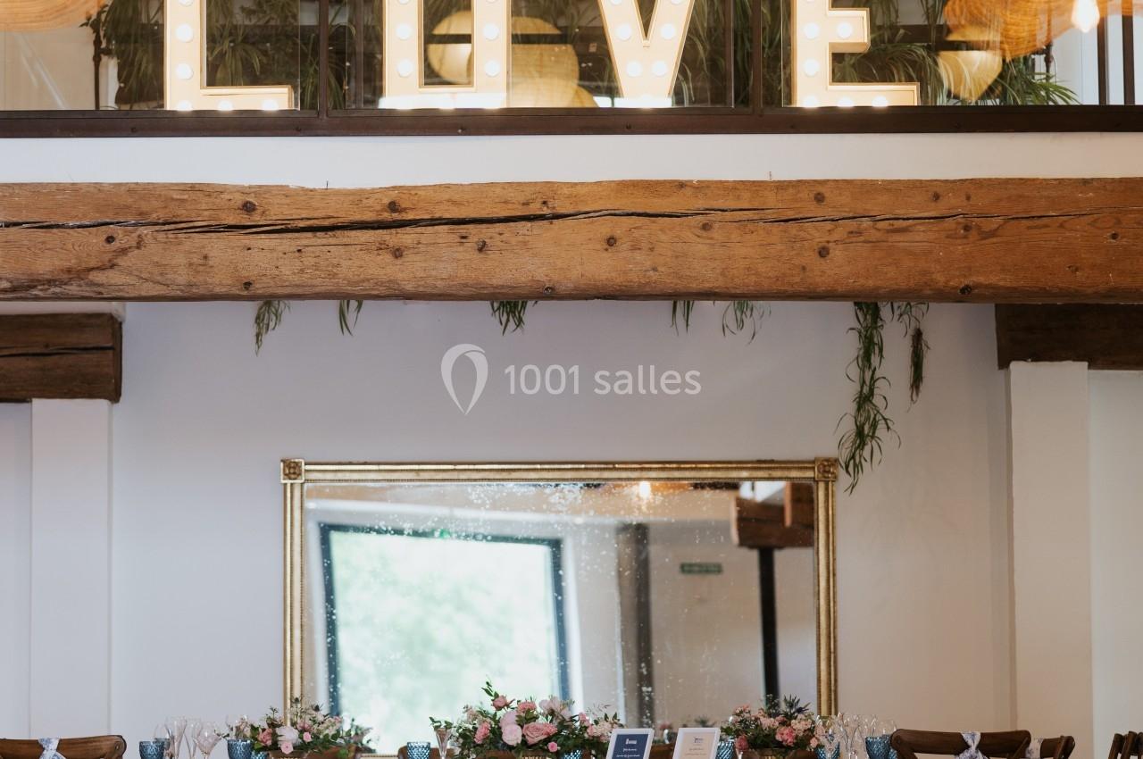 Salle décorée pour un événement avec une table ornée de fleurs et le mot ’LOVE’ illuminé en arrière-plan.