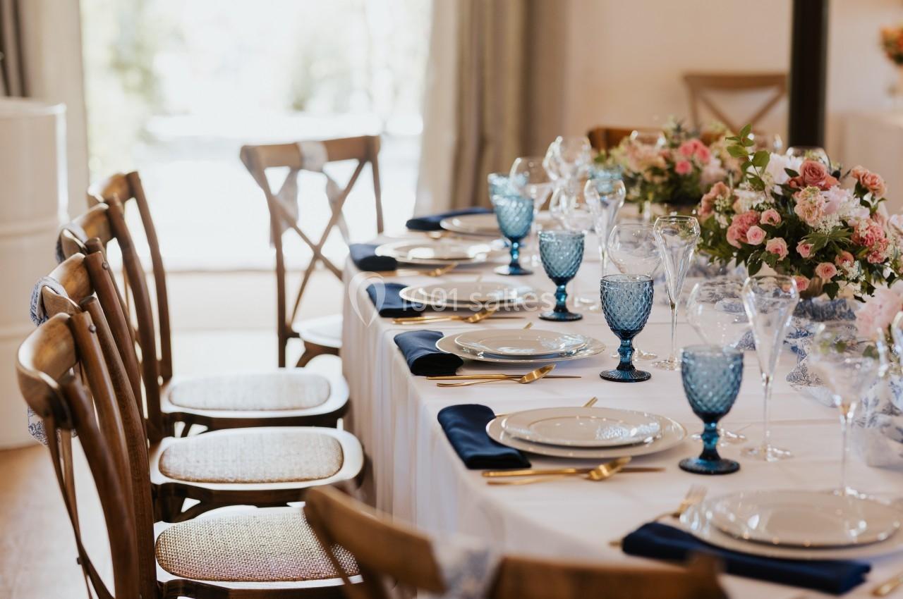 Table élégamment dressée avec vaisselle blanche, verres bleus, serviettes bleu marine et bouquets de fleurs roses.