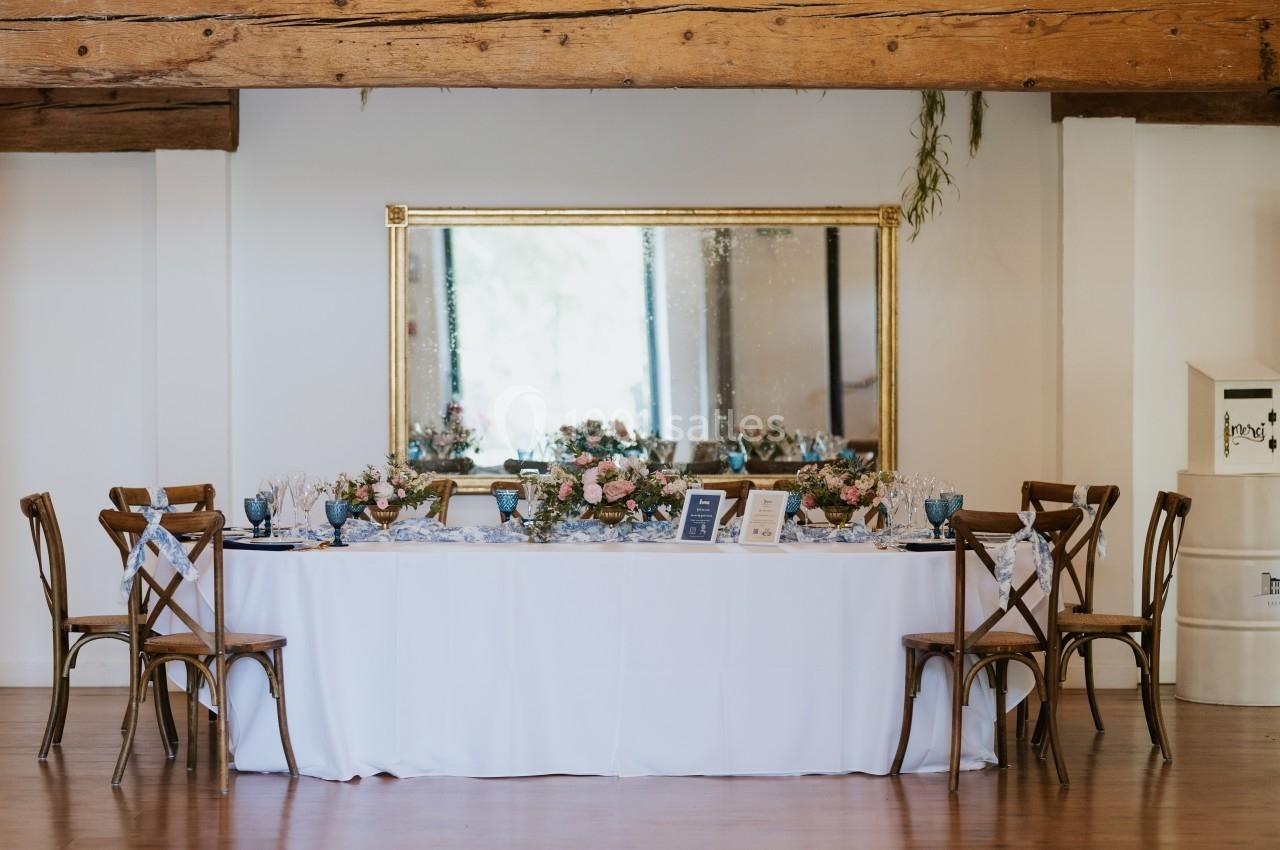 Table élégamment dressée avec des fleurs et des verres, entourée de chaises en bois, devant un grand miroir doré.