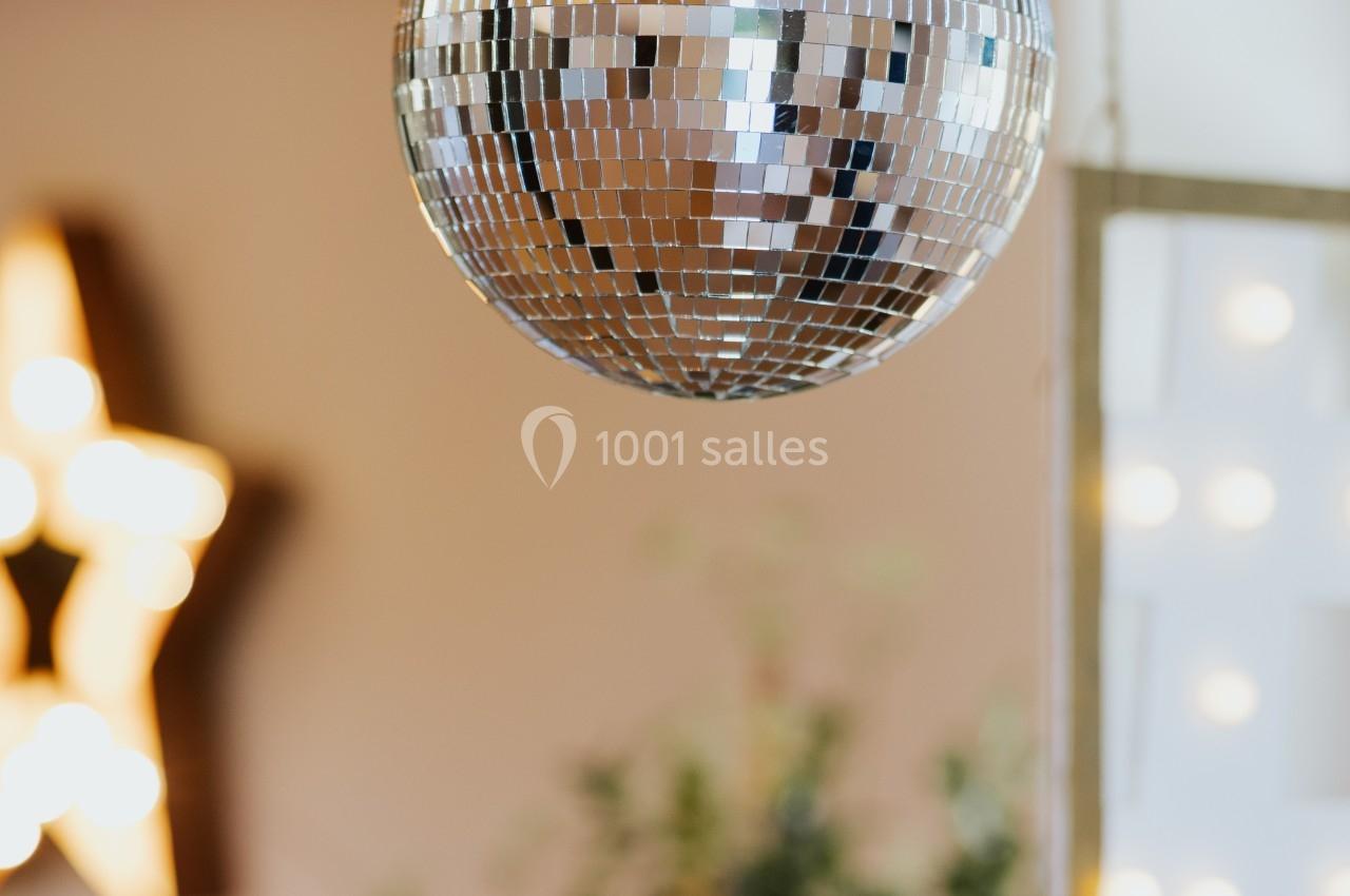 Boule à facettes suspendue dans une pièce lumineuse avec des décorations floues en arrière-plan.