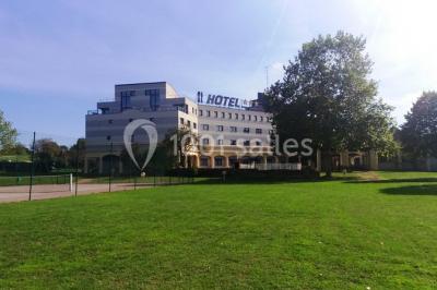 Salon lumineux avec canapé beige, table basse en bois, escalier, grande baie vitrée et vue sur un paysage extérieur.