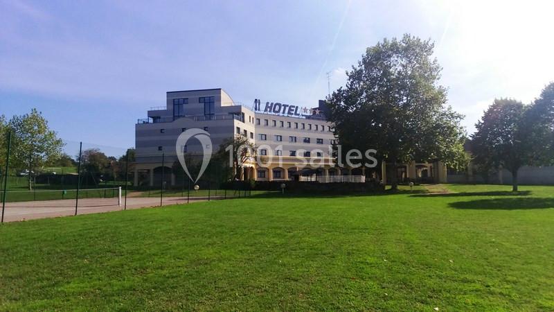 Bâtiment d'un hôtel moderne entouré de pelouses et d'arbres, sous un ciel dégagé.
