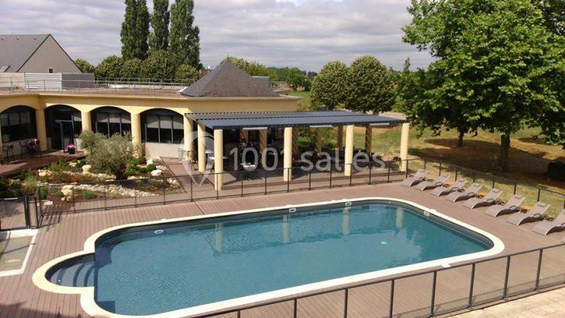 Piscine extérieure entourée d'une terrasse en bois, avec transats et bâtiment en arrière-plan.