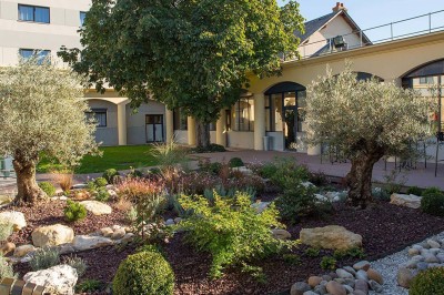 Salon lumineux avec canapé beige, table basse en bois, escalier, grande baie vitrée et vue sur un paysage extérieur.