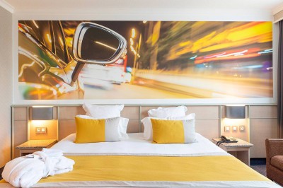 Salon lumineux avec canapé beige, table basse en bois, escalier, grande baie vitrée et vue sur un paysage extérieur.