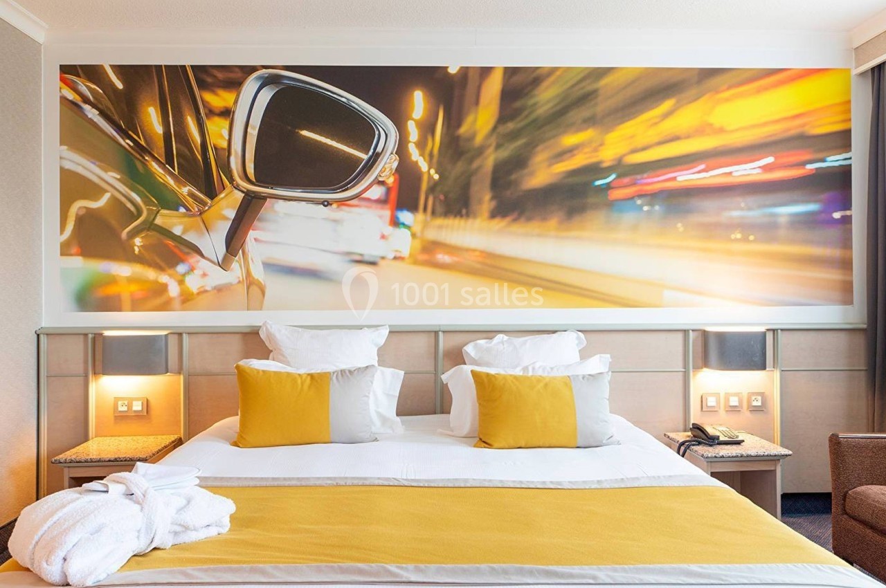 Lit double avec coussins jaunes dans une chambre moderne, décorée d'une grande photo murale de voiture en mouvement.