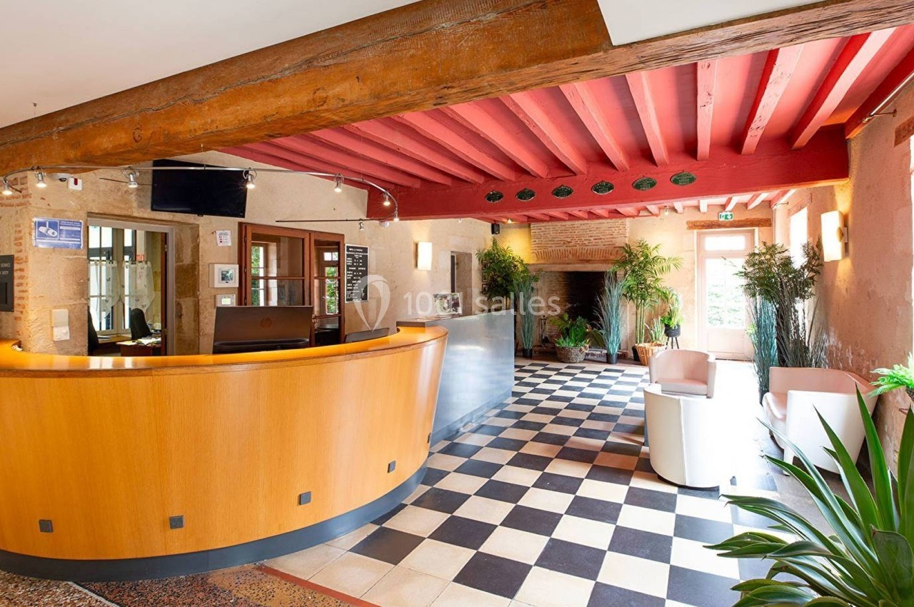 Accueil d'un bâtiment avec comptoir en bois courbé, sol en damier, poutres apparentes et plantes décoratives.