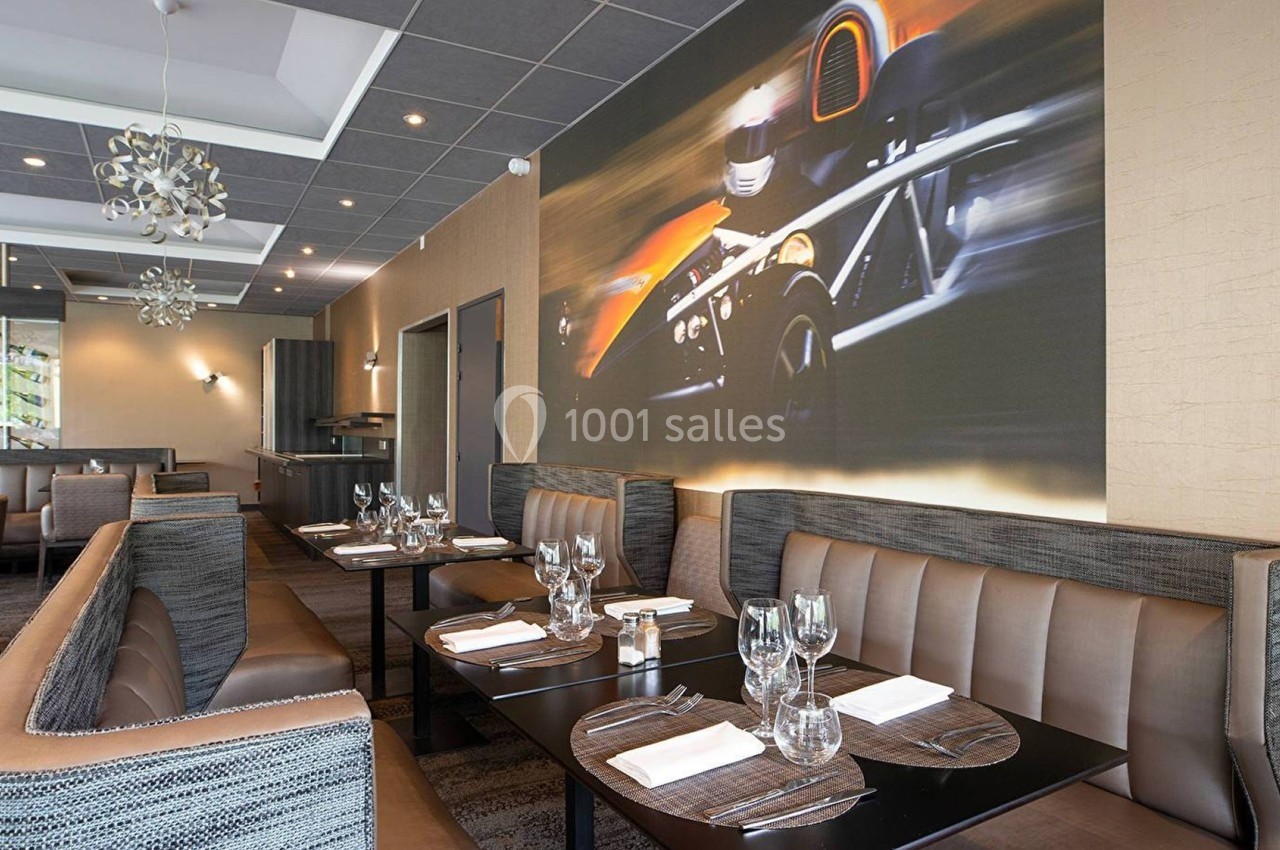 Salle de restaurant moderne avec banquettes, tables dressées et une grande fresque murale représentant une voiture de course.