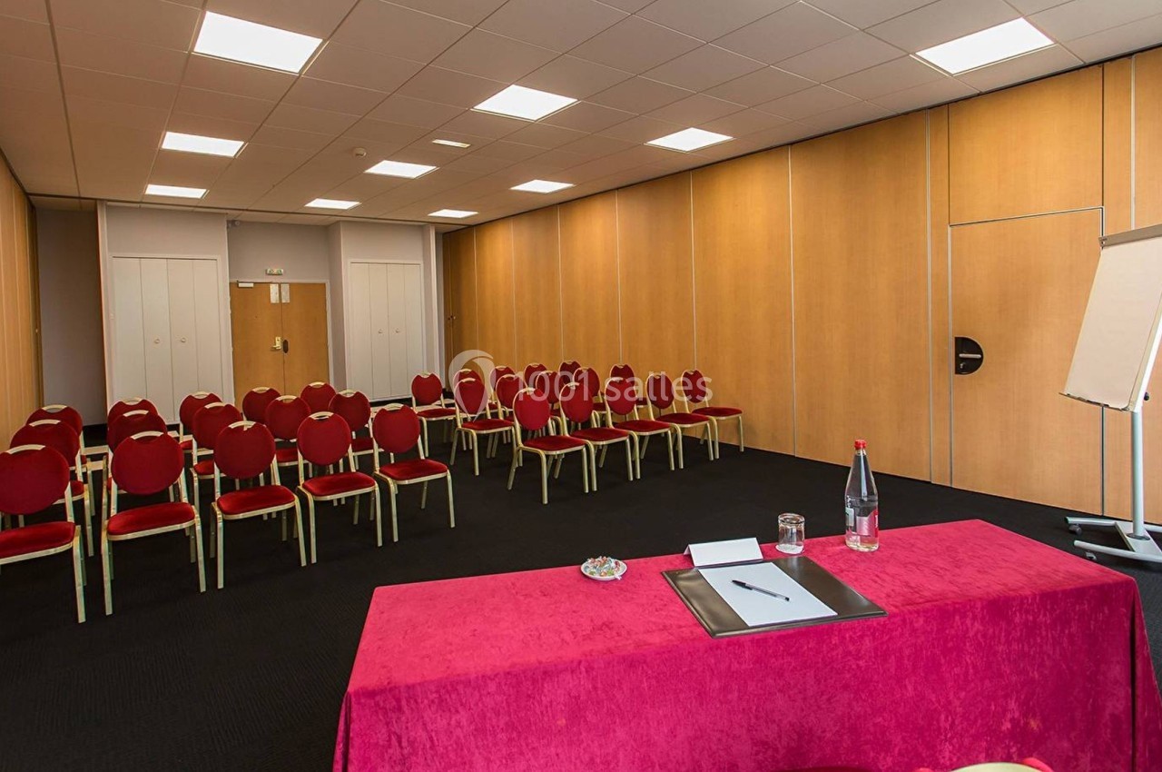 Salle de réunion avec chaises rouges alignées, table recouverte d'une nappe rouge et tableau de conférence blanc.