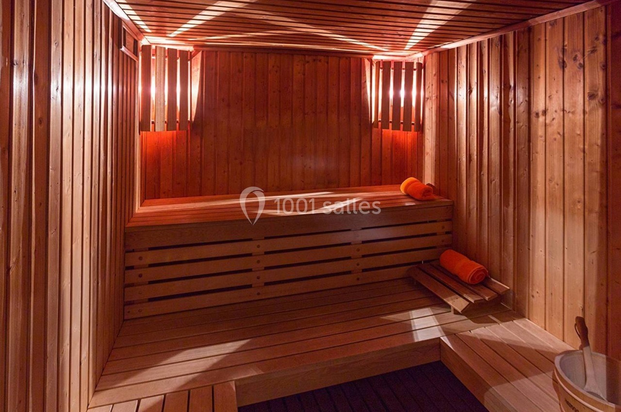 Sauna en bois avec bancs, lumière tamisée et serviettes orange pliées.