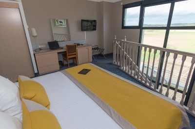 Salon lumineux avec canapé beige, table basse en bois, escalier, grande baie vitrée et vue sur un paysage extérieur.