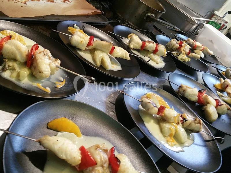 Brochettes de poisson et légumes servies sur des assiettes noires avec une sauce et des morceaux d'orange.