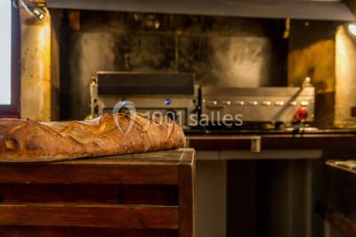 Baguette de pain posée sur un comptoir en bois, avec un four professionnel en arrière-plan dans une cuisine.