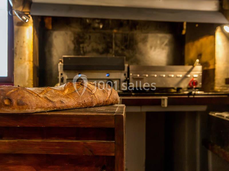 Baguette de pain posée sur un comptoir en bois, avec un four professionnel en arrière-plan dans une cuisine.