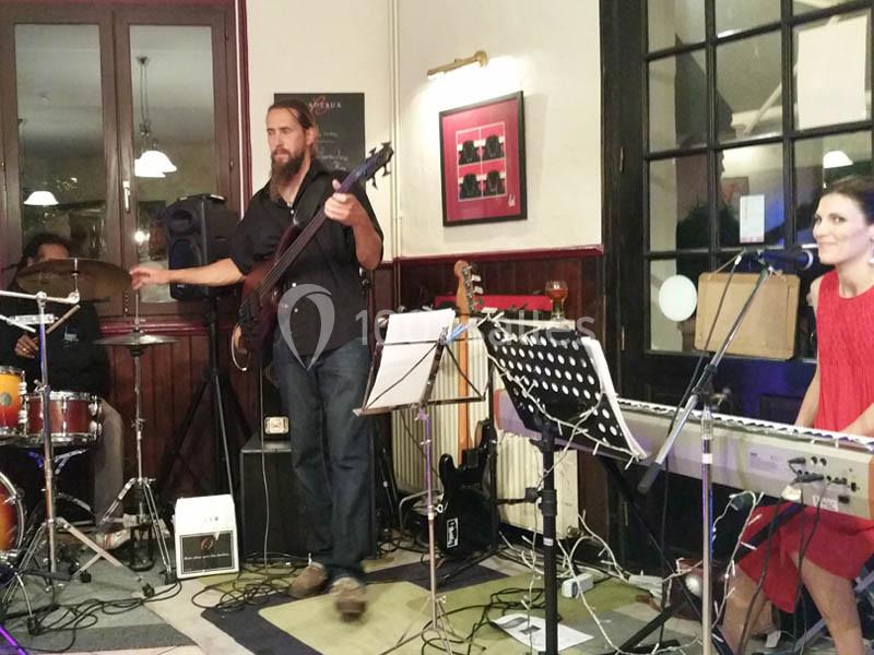 Un groupe de musiciens joue en intérieur, avec un bassiste, une pianiste-chanteuse et un batteur.