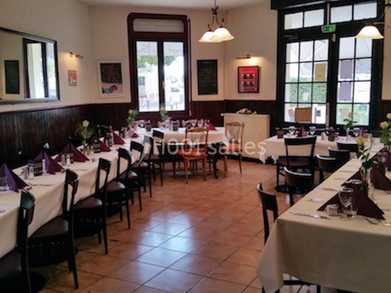 Salle de restaurant lumineuse avec tables dressées, nappes blanches et serviettes violettes, prête à accueillir des convives.