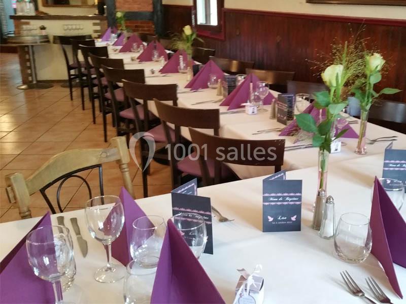Tables dressées avec nappes blanches, serviettes violettes pliées, verres et décorations florales dans une salle de…