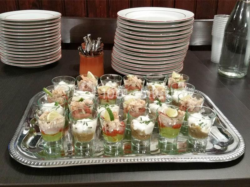 Plateau de verrines variées avec des ingrédients colorés, disposé sur une table près d'assiettes empilées.