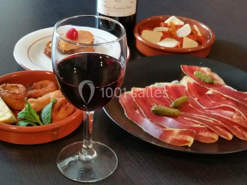 Assiette de jambon cru, tapas variées et verre de vin rouge sur une table sombre.