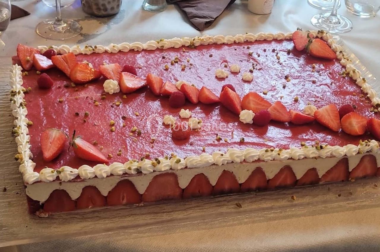 Gâteau rectangulaire décoré de fraises, framboises, chantilly et éclats de pistaches sur une table dressée.