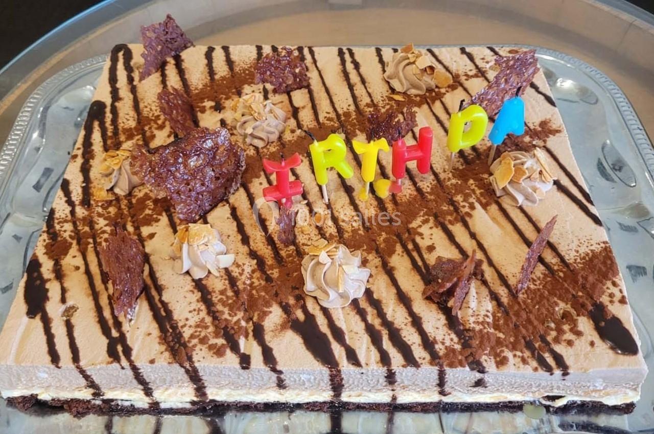 Gâteau rectangulaire décoré de chocolat, crème et lettres colorées formant ’BIRTHDAY’.