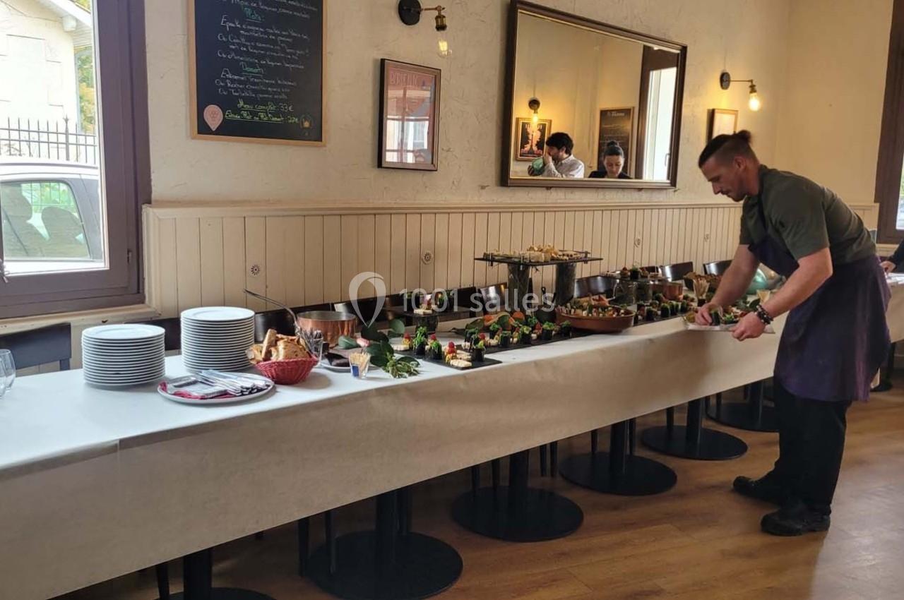 Un buffet avec des plats variés, des assiettes empilées et un homme en tablier disposant des aliments.