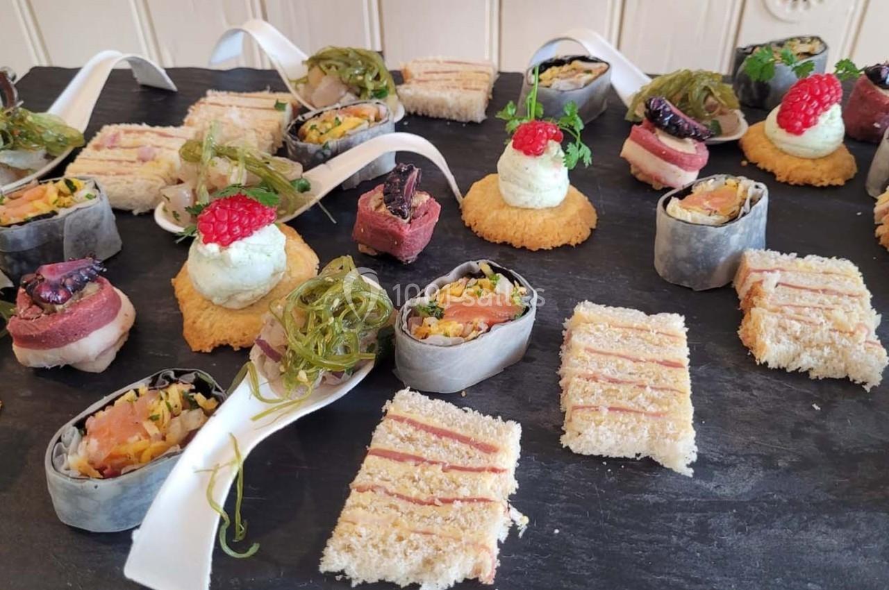 Plateau de bouchées variées comprenant sushis, toasts, mousse et garnitures colorées sur une ardoise noire.