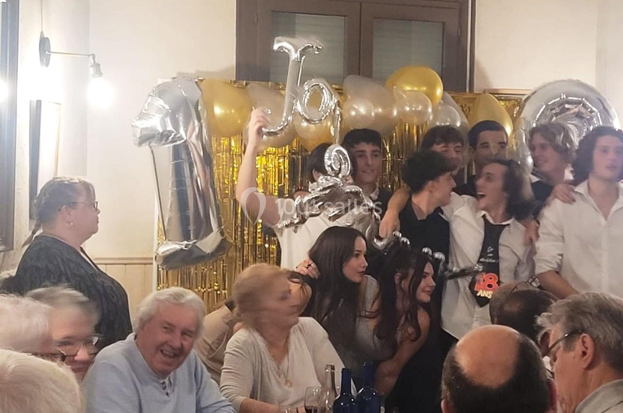 Un groupe de jeunes et d'adultes réunis lors d'une fête, avec des ballons dorés et argentés en arrière-plan.