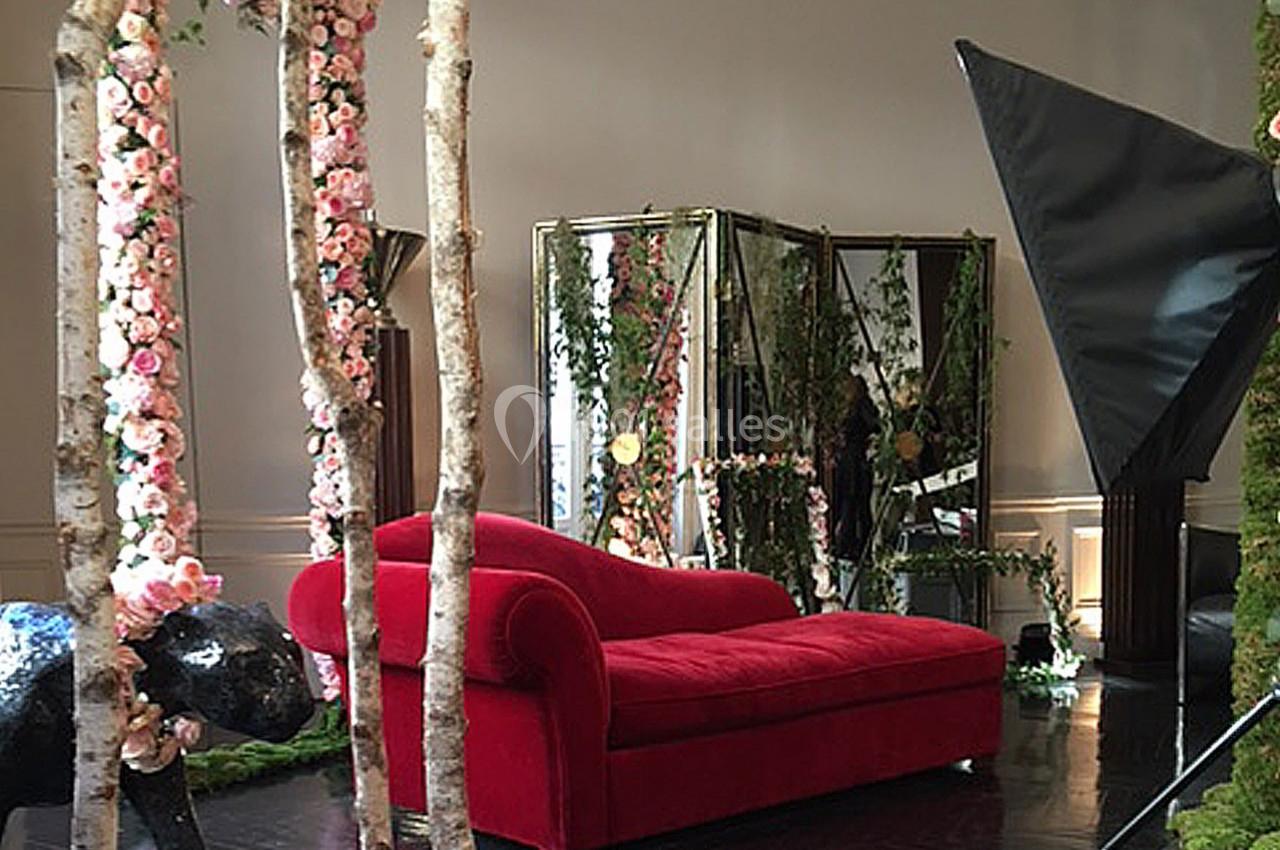 Canapé rouge entouré de décorations florales, miroirs et accessoires de studio photo dans un espace intérieur.